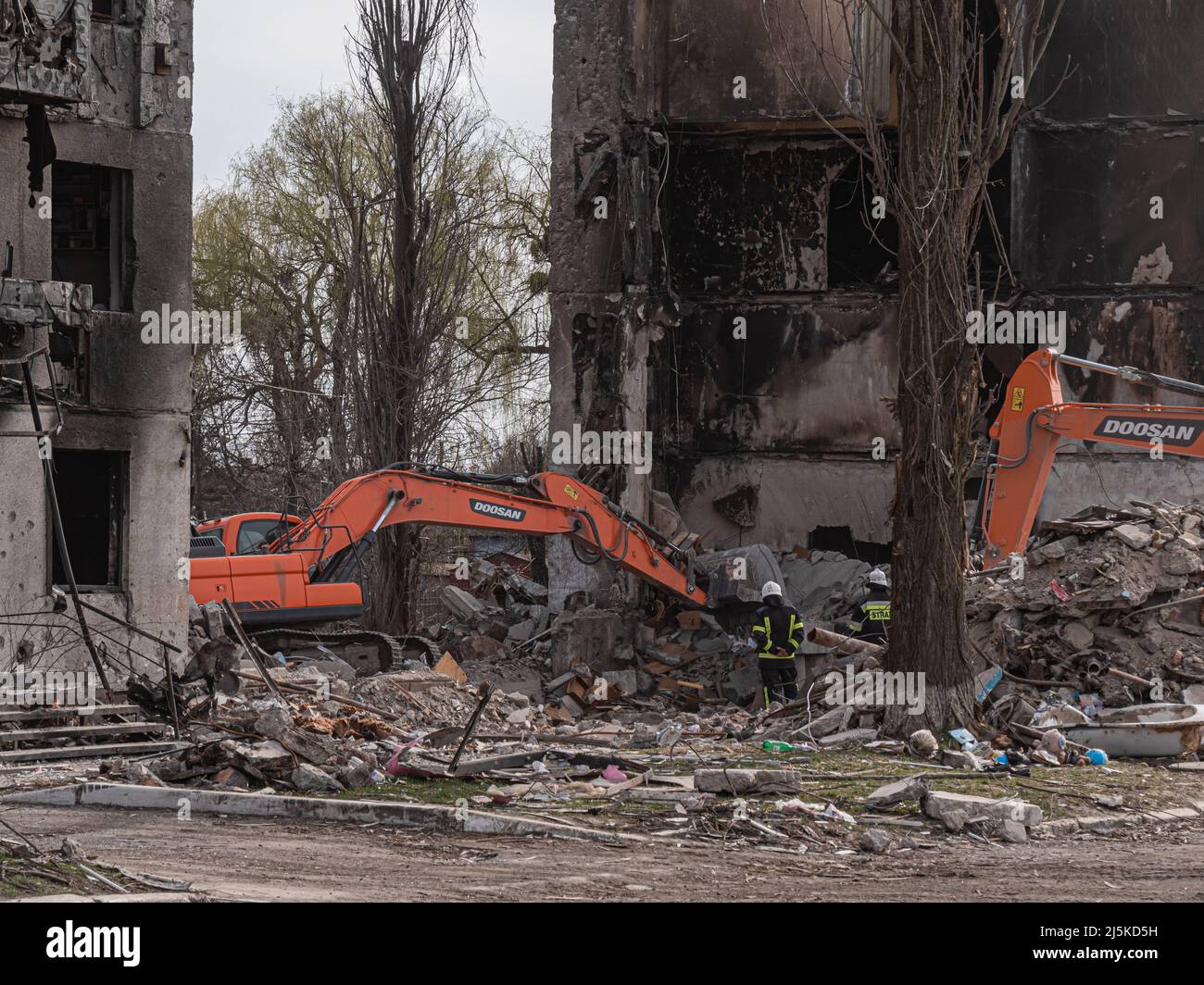 Borodyanka, Ucrania - abril de 2022: Vista de la excavadora que trabaja sobre los escombros de edificios residenciales. Limpieza de desechos en busca de personas heridas por bombardeos aéreos. Casas destruidas después de los ataques con cohetes. Foto de stock