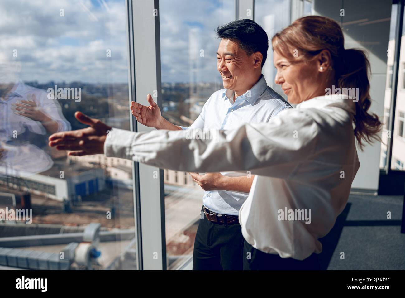 feliz mujer segura está mostrando a su socio de negocios asiático su proyecto en ventana Foto de stock