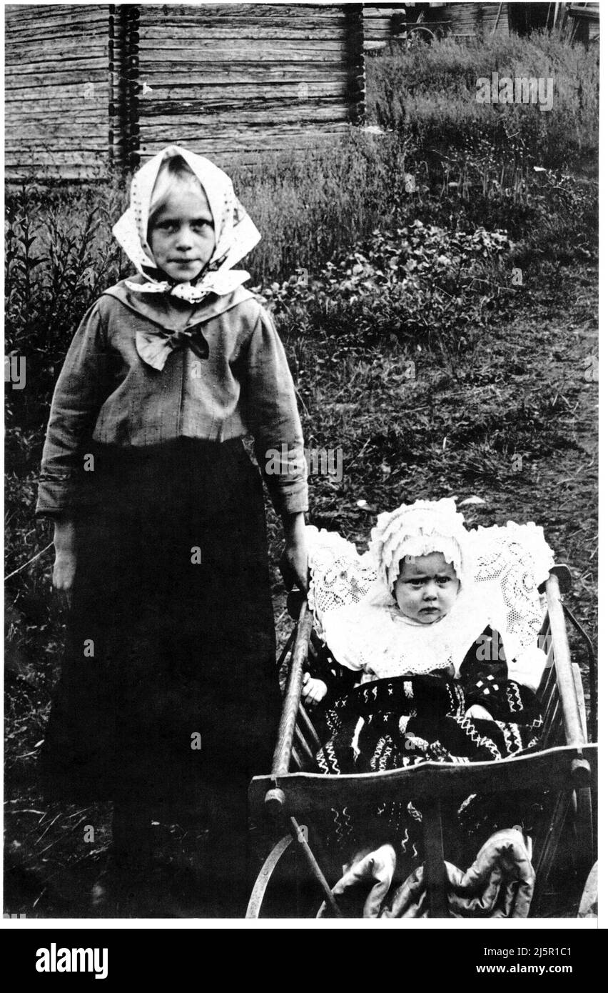 Fotografía vintage auténtica de 1910 de niño de pie y bebé en carrito de madera al aire libre mirando a la cámara, Suecia, Escandinavia Foto de stock