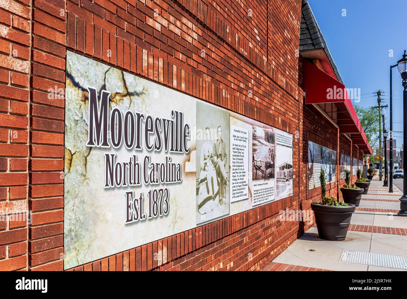 MOORESVILLE, NC, EE.UU.-17 DE ABRIL de 2022: Pared de ladrillo largo en la calle principal con fotografías históricas y señales de información. Imagen en perspectiva diagonal. Foto de stock