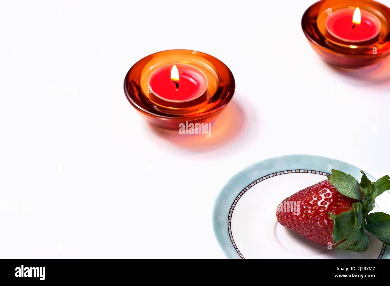Velas rojas encendidas para meditar antes de comer una fresa grande y deliciosa. Foto de stock