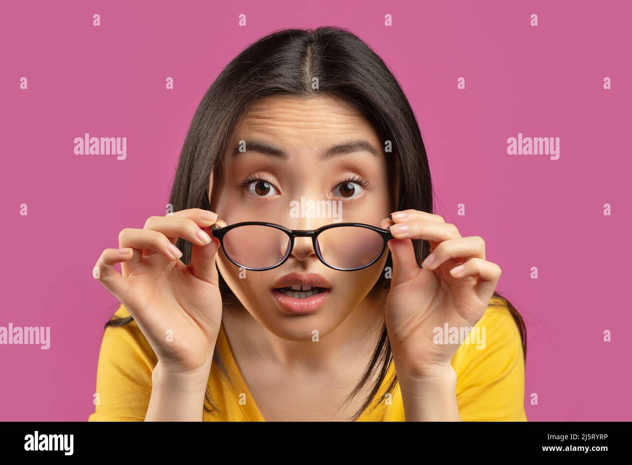 Mala vista. Mujer asiática que lleva gafas y mira la cámara encima de los  anteojos, de pie sobre fondo de estudio violeta Fotografía de stock - Alamy