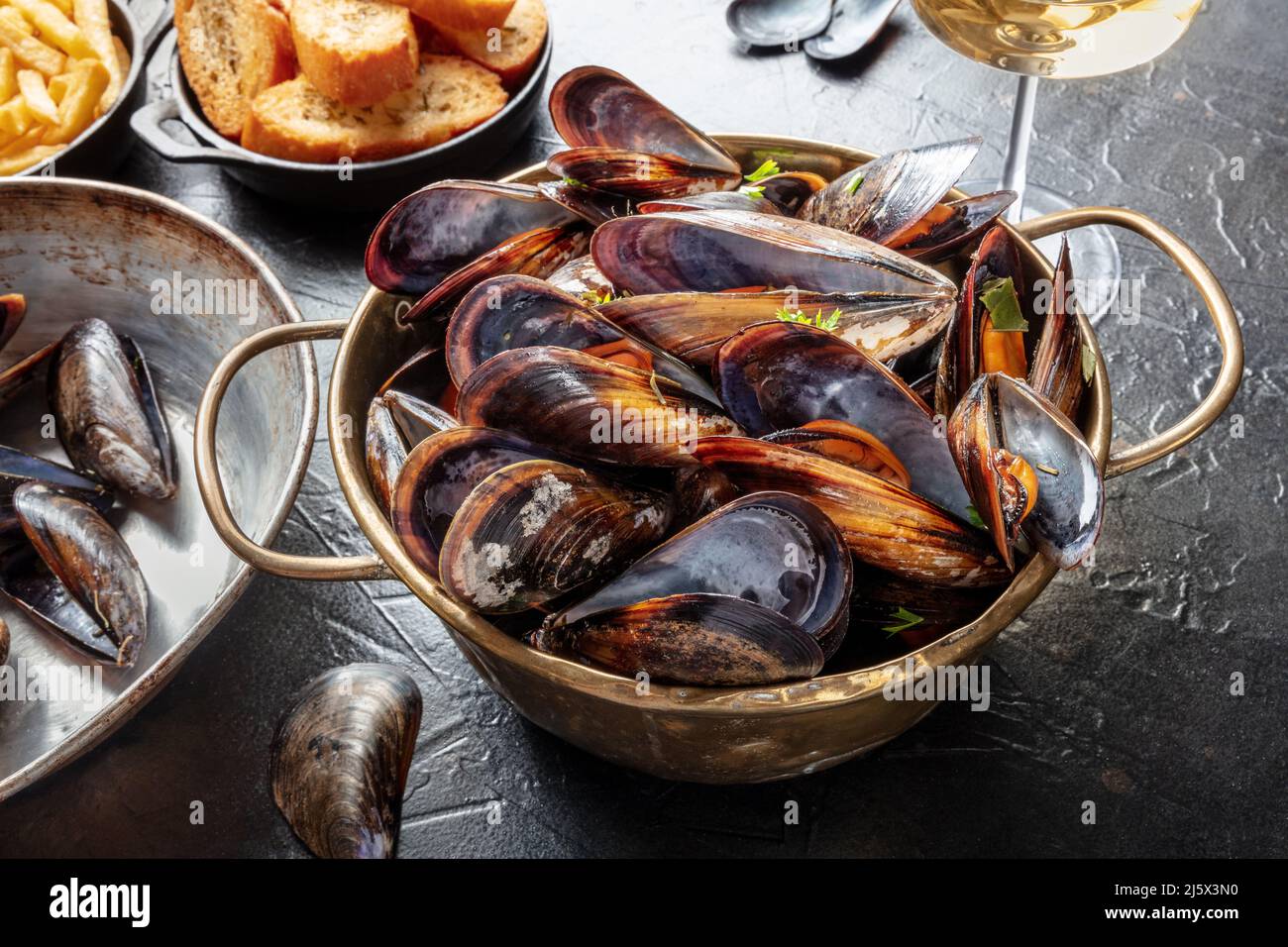 Cena de mejillones en un restaurante francés, con vino y pan tostado, sobre una mesa oscura Foto de stock