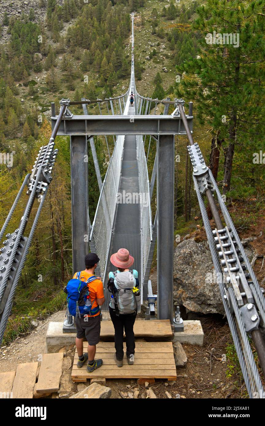 Dos excursionistas miran la única cuadrícula de 65 centímetros de ancho del puente colgante Charles Kuonen, Randa, Valais, Suiza Foto de stock