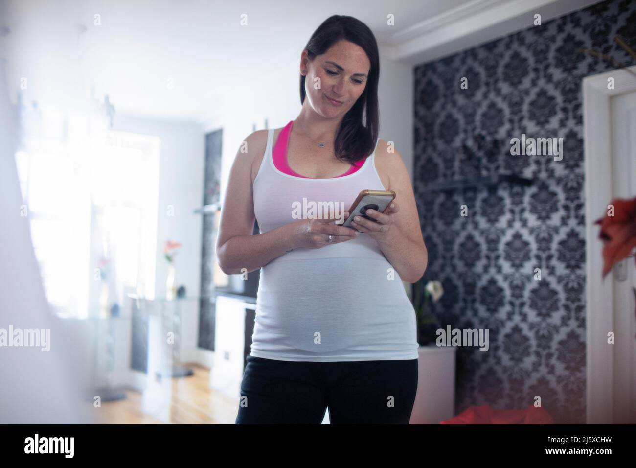 Mujer embarazada en la parte superior del tanque usando un teléfono inteligente Foto de stock