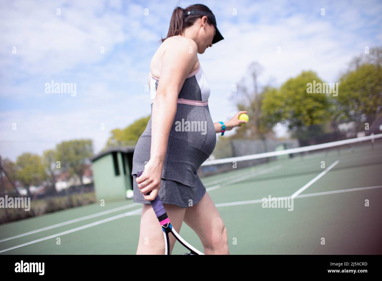 Mujer embarazada jugando al tenis en la soleada pista de tenis Foto de stock