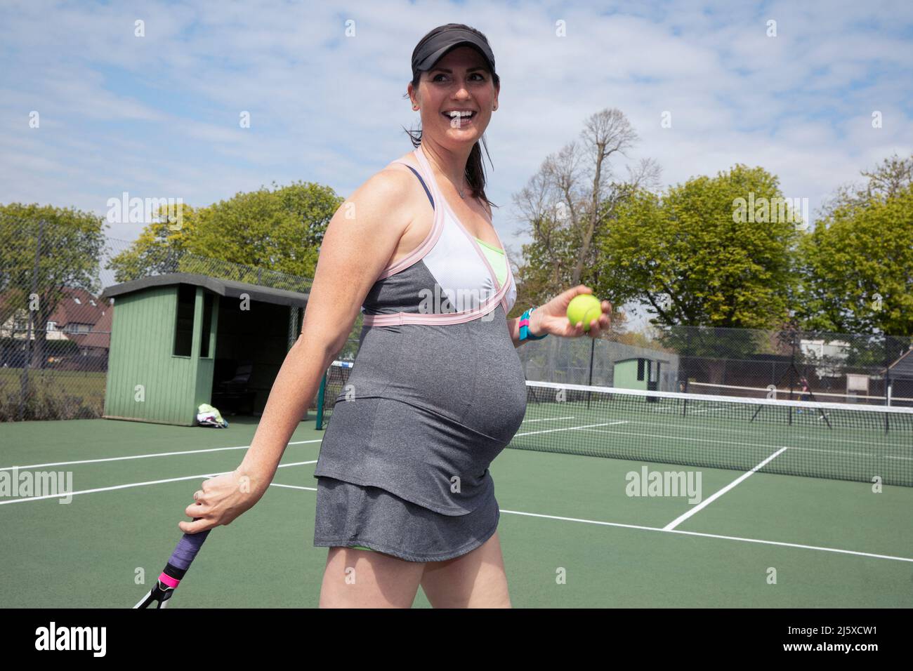 Feliz mujer embarazada jugando al tenis en la soleada pista de tenis Foto de stock