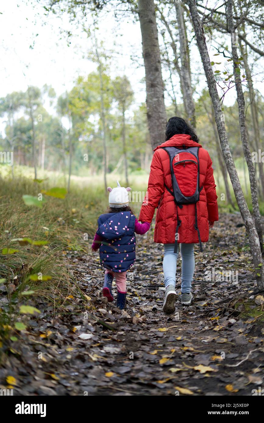 Madre e hija sosteniendo las manos caminando por el sendero en el bosque Foto de stock