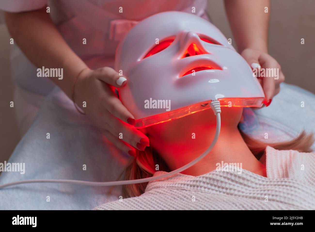 Máscara ANTI-envejecimiento con luz LED para el cuidado facial de la piel  en un spa a cámara lenta. Una mujer se acuesta en un sofá en una máscara  especial. Tecnologías modernas de