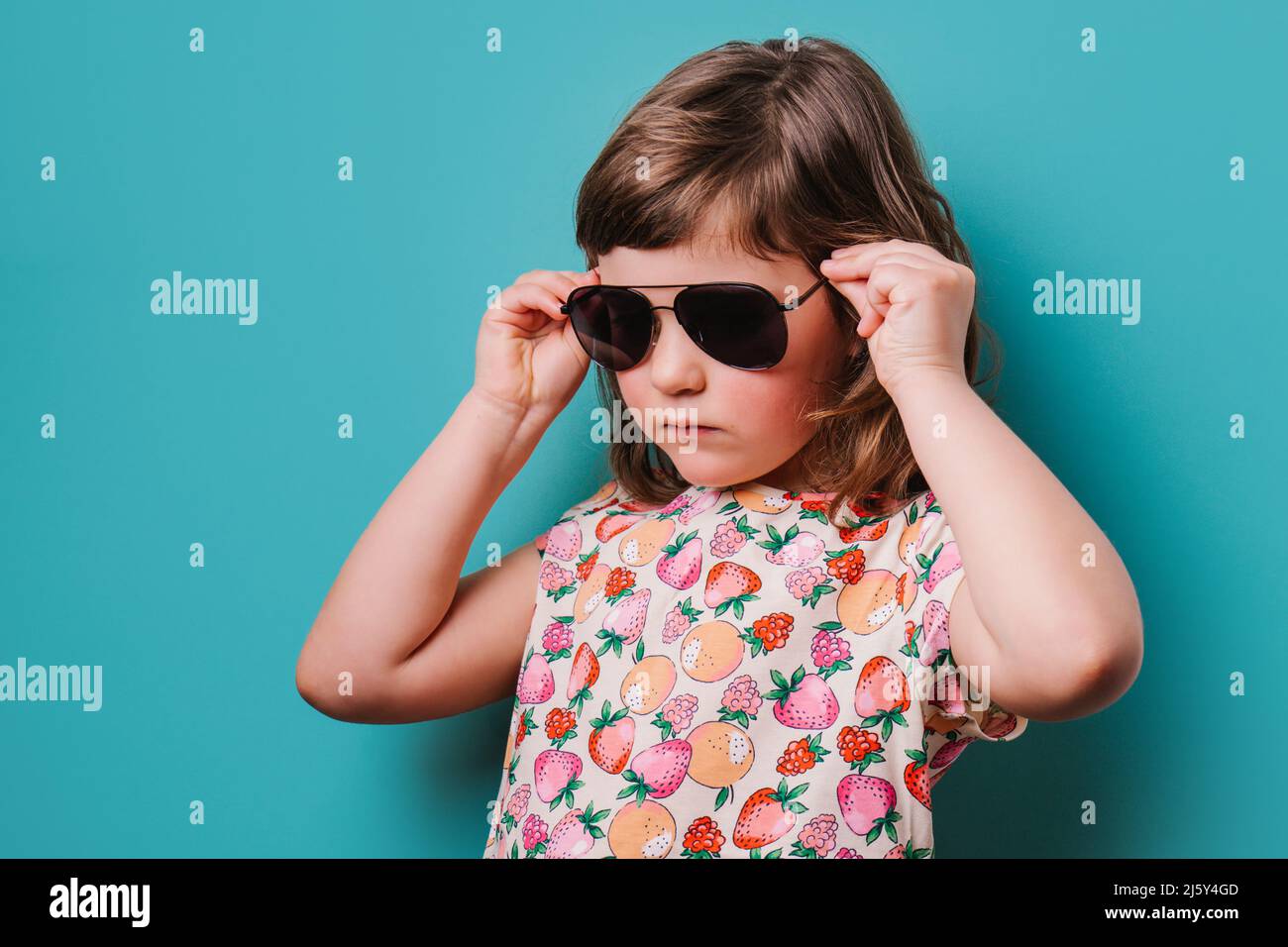 Chica seria con estilo colorido ponerse gafas de sol negro de moda mientras  que de pie sobre fondo turquesa en un moderno estudio de luz Fotografía de  stock - Alamy