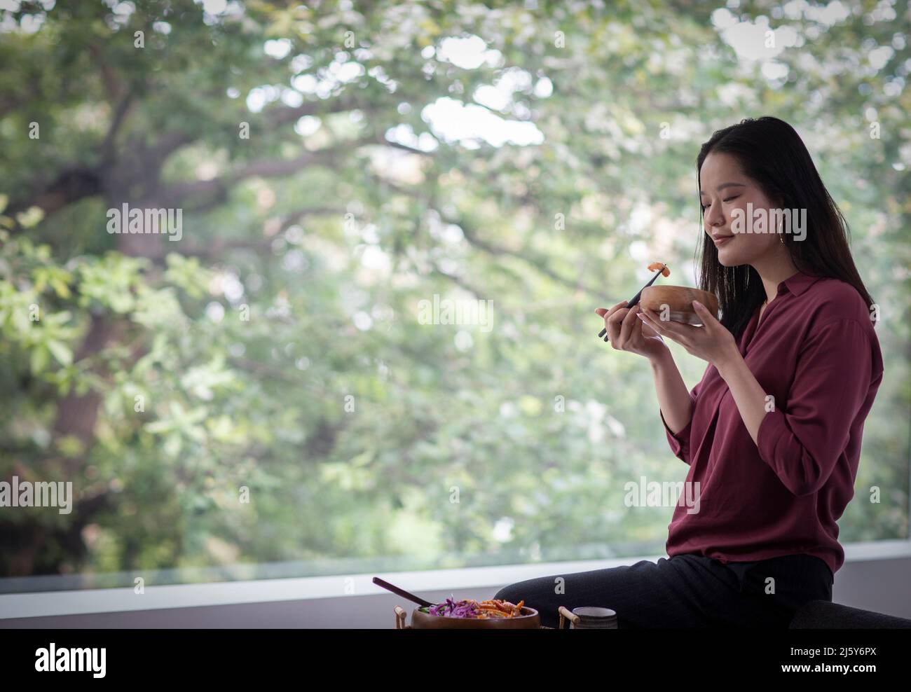 Mujer joven comiendo con palillos en la ventana Foto de stock