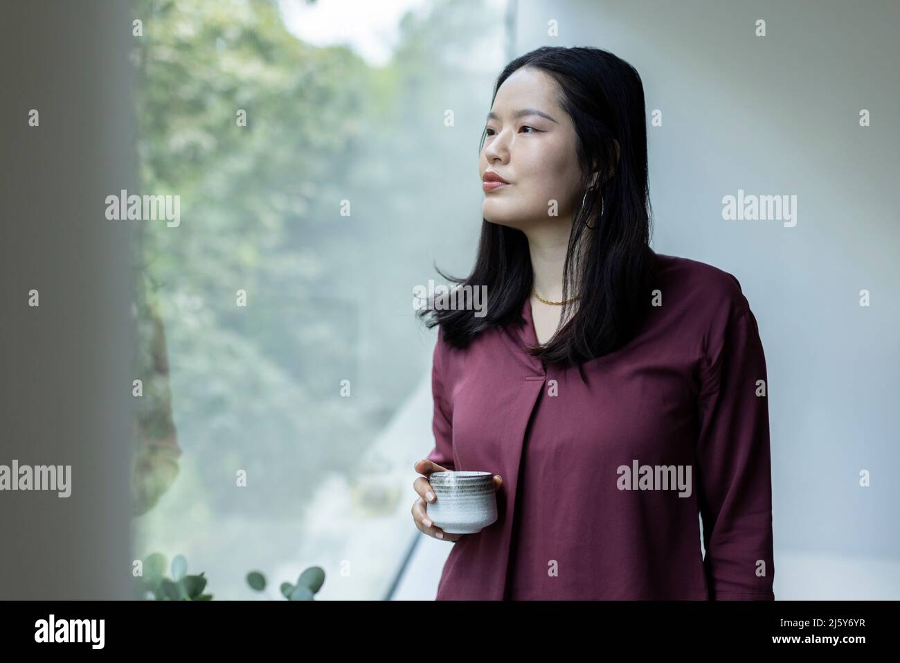 Una mujer joven muy atenta bebiendo té en la ventana Foto de stock
