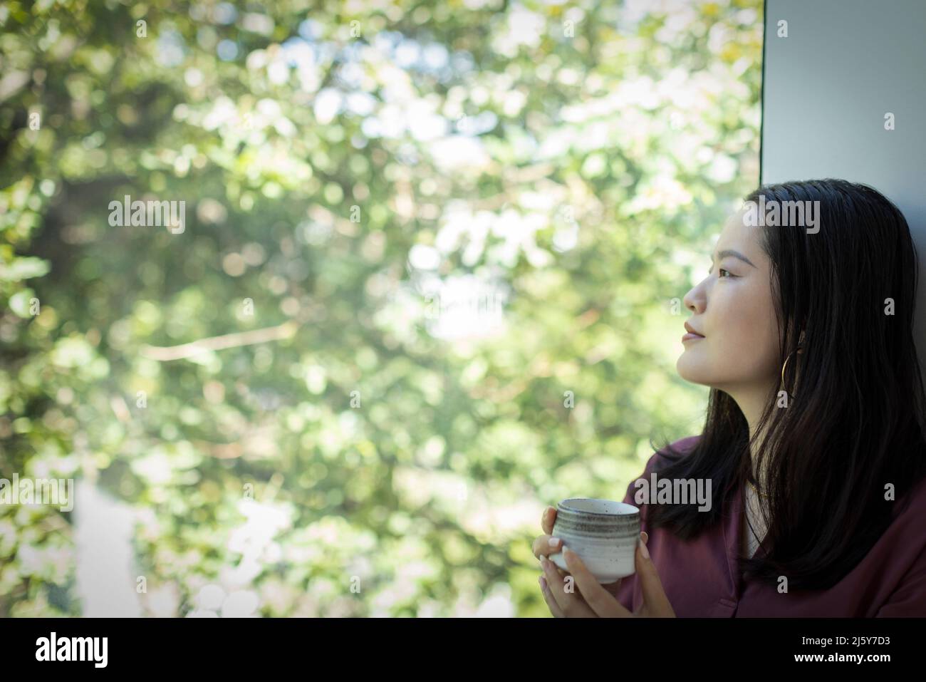 Una mujer joven muy atenta bebiendo té y mirando por la ventana Foto de stock