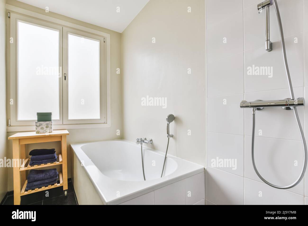 Bañera blanca de cerámica con manguera de ducha colocada en la pared de  azulejos en un baño luminoso con estante cerca de una pequeña ventana en  casa Fotografía de stock - Alamy