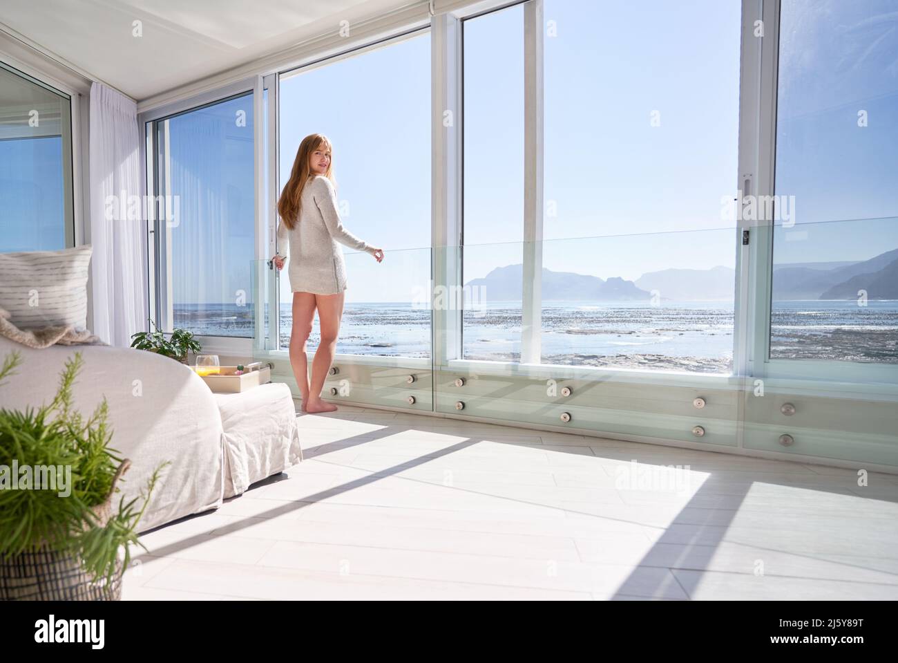 Retrato joven de pie en la puerta abierta del patio con vista soleada al océano Foto de stock