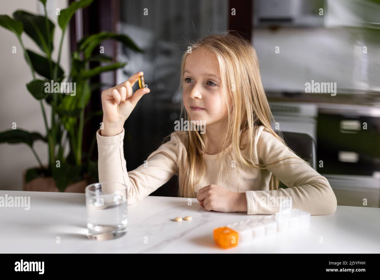Niña Caucásica en pijamas tomando vitamina omega-3 natural de la caja de  plástico en la cocina en casa temprano por la mañana. Un niño adorable toma  suplementos Fotografía de stock - Alamy