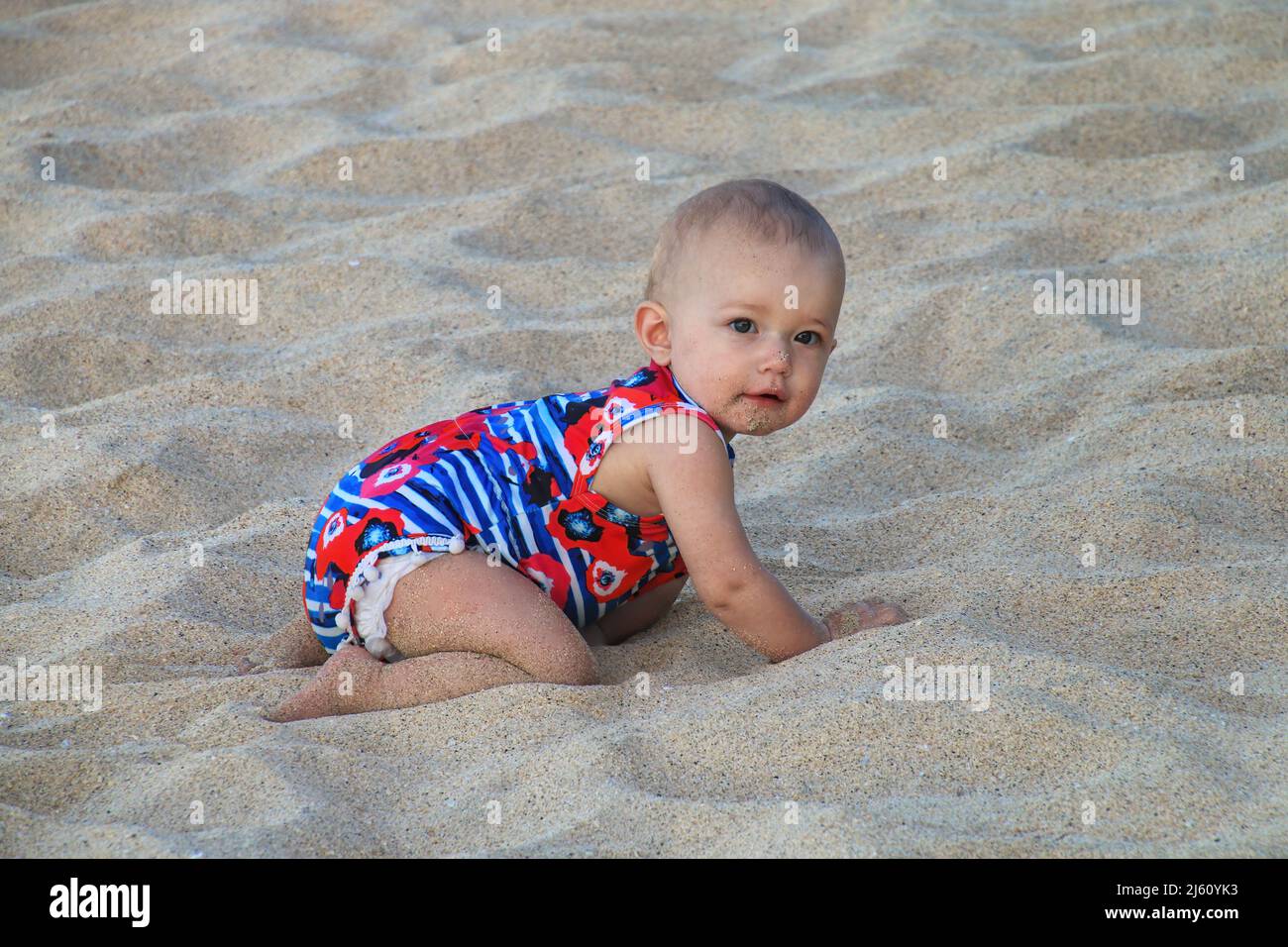 Bebé niña arrastrándose en una suave arena de playa Foto de stock