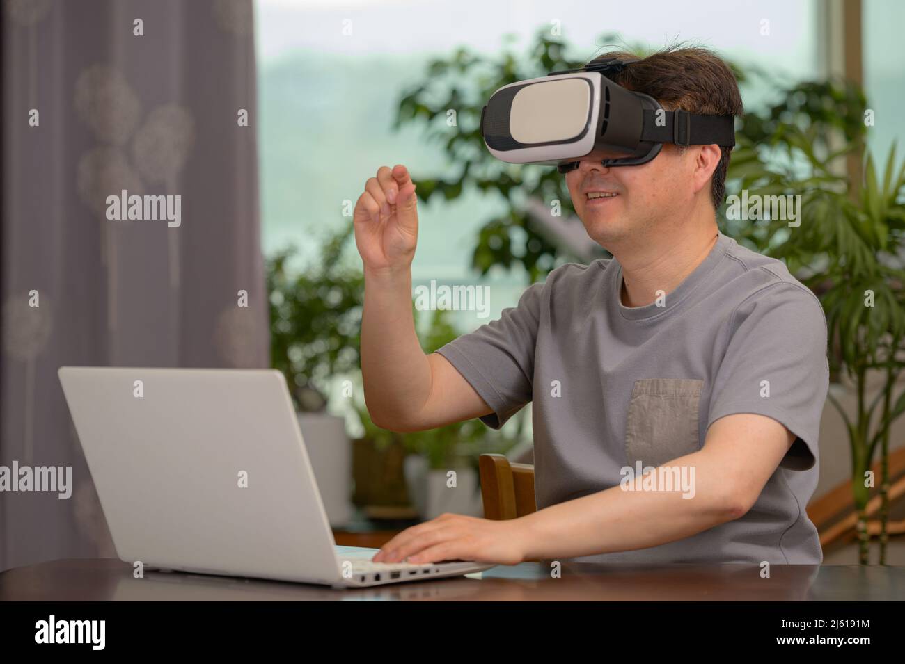 Hombre asiático con auriculares VR y portátil sentado en su escritorio Foto de stock
