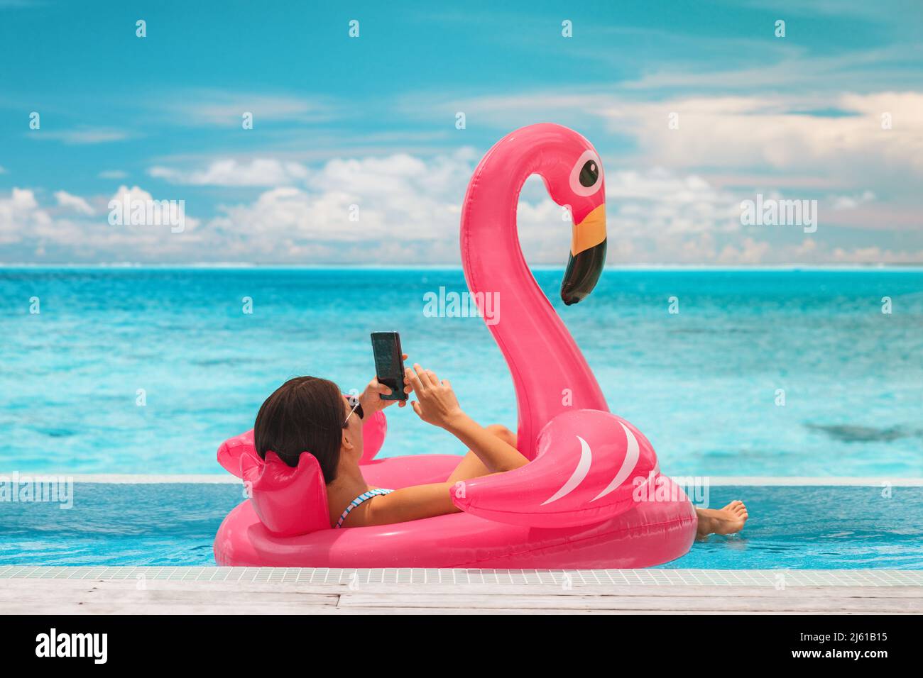 Vacaciones en verano piscina relajante mujer flotando en flotadores inflables flamencos usando el teléfono móvil en un resort de lujo para tomar el sol. Viajes al Caribe Foto de stock