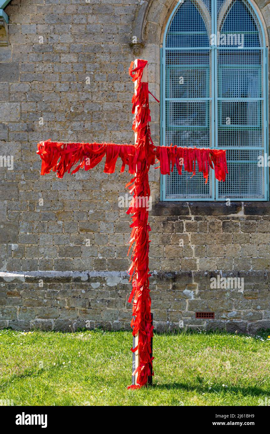 Cruz de Pascua decorada con cintas rojas fuera de una iglesia en Haslemere, Surrey, Inglaterra, Reino Unido. El rojo representa la sangre del cordero de Dios, Jesucristo Foto de stock