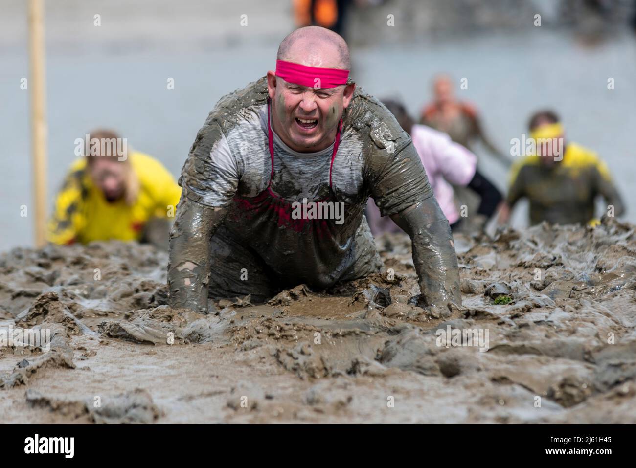 Hombre arrastrándose en el barro en la Maldon Mud Race 2022 en el río Blackwater, Essex, Reino Unido. Foto de stock