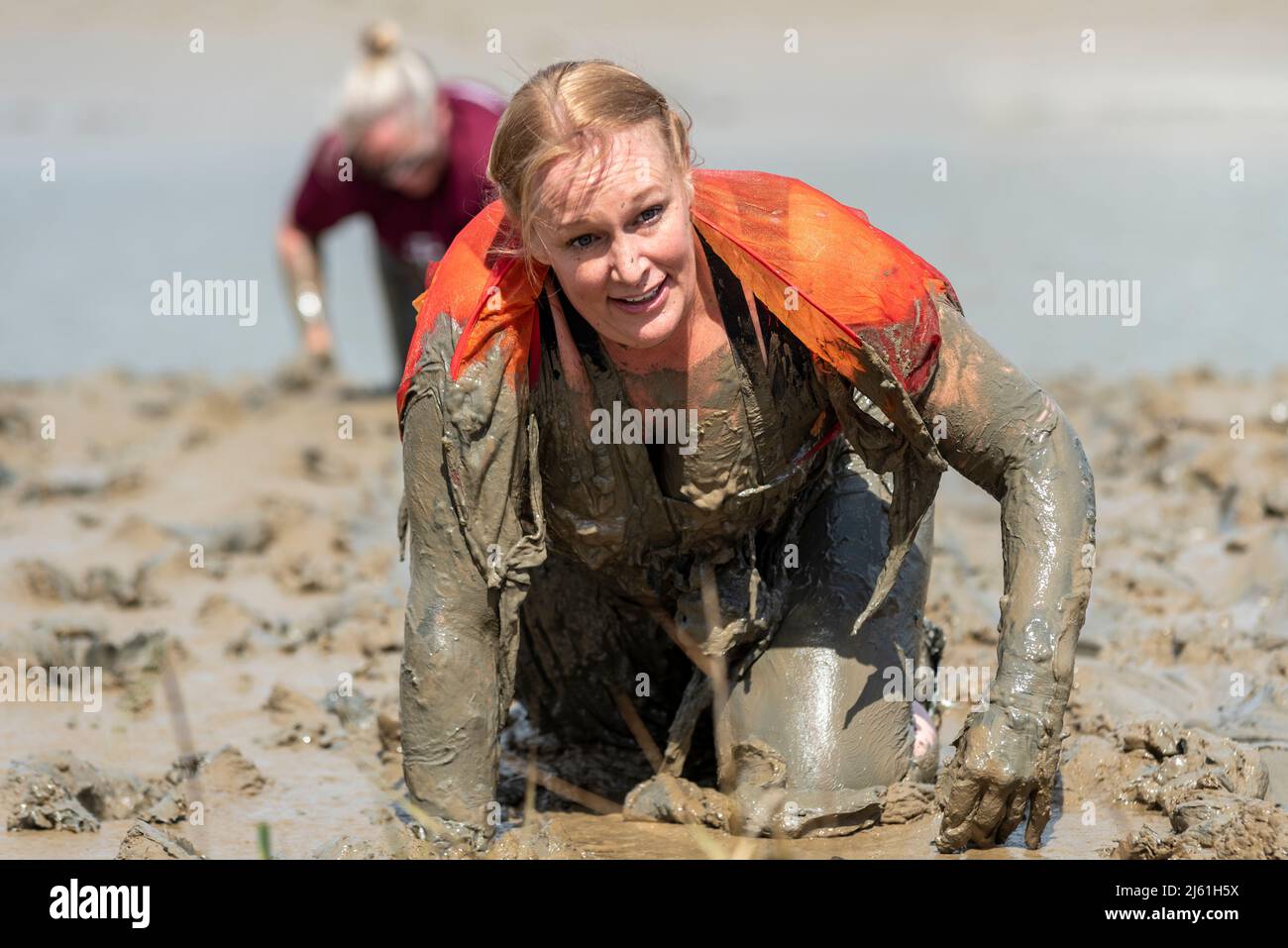 Mujer arrastrándose en el barro en la Maldon Mud Race 2022 en el río Blackwater, Essex, Reino Unido. Foto de stock