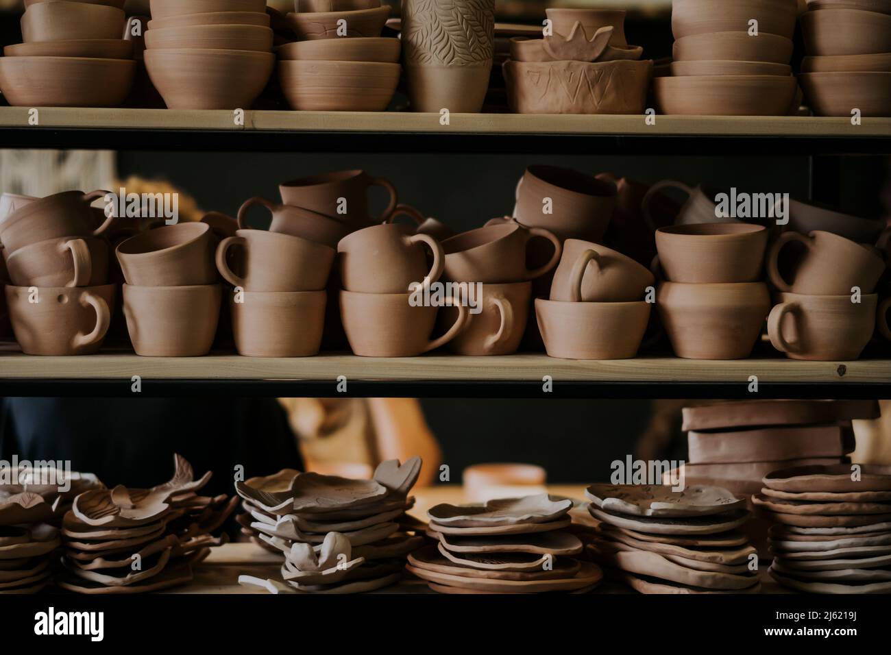 Tazones de cerámica hechos a mano con tazas y platos en el estante en el taller Foto de stock