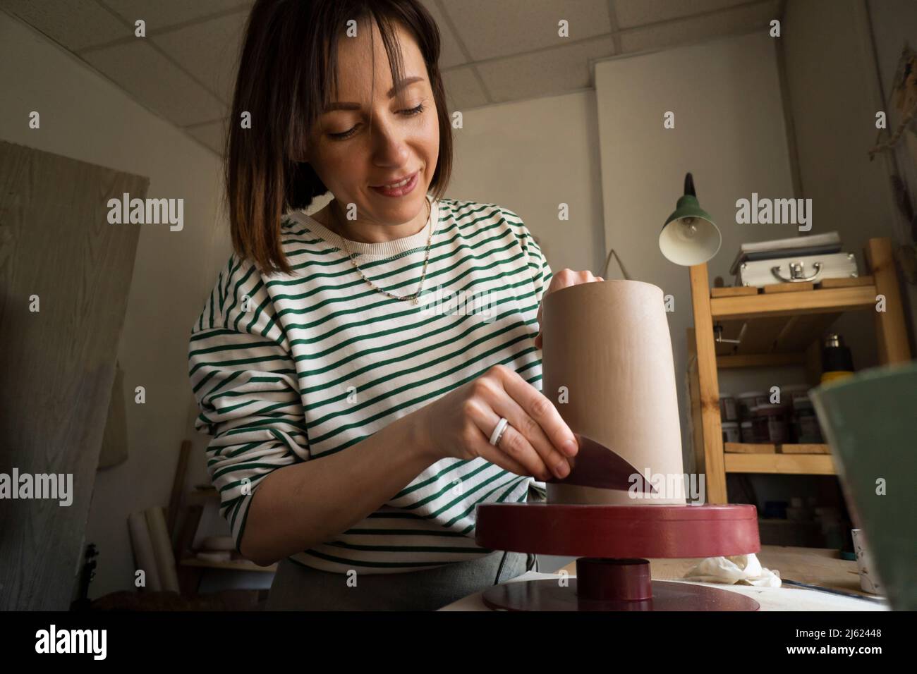 Mujer moldeando cerámica con herramienta de mano en el taller Foto de stock