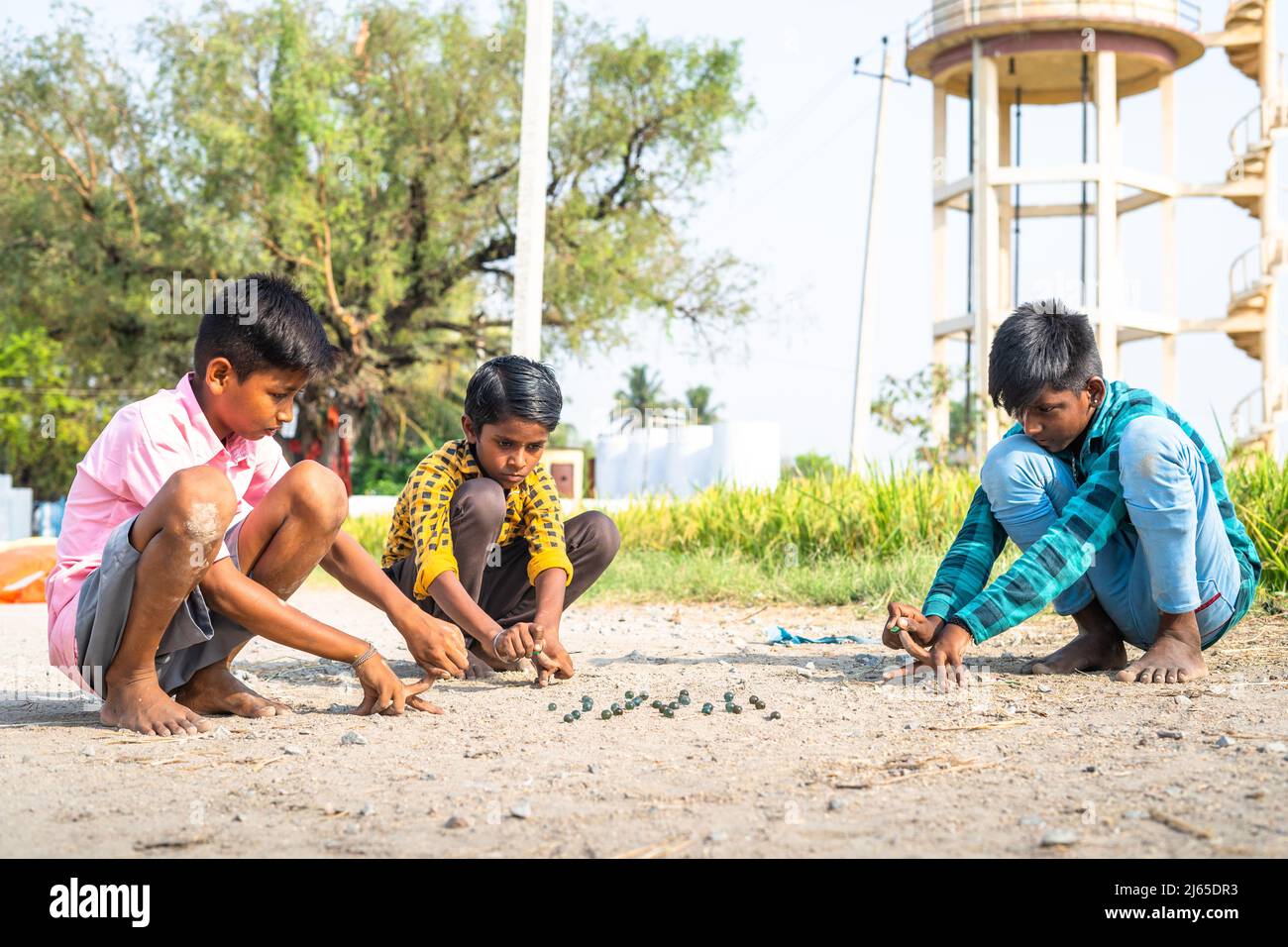 Los niños de la aldea india que juegan goli o mármoles en el campo de arroz cercano - concepto de juego tradicional, vacaciones de verano y actividades de ocio. Foto de stock