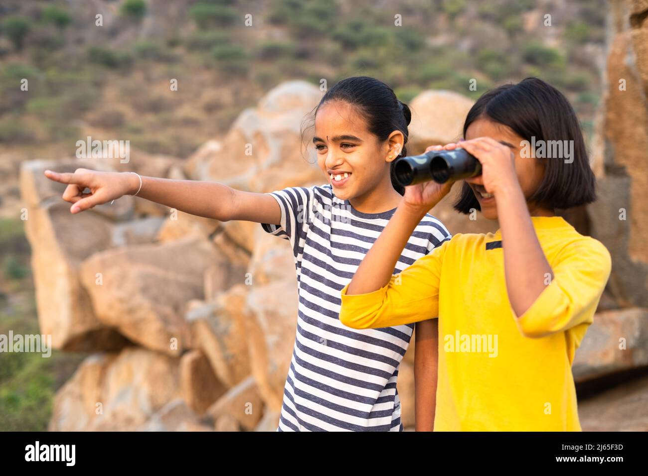 Niñas niños viendo lejos utilizando binocular en la cima de la montaña durante el campamento de verano - concepto de vacaciones, expedición y disfrute Foto de stock