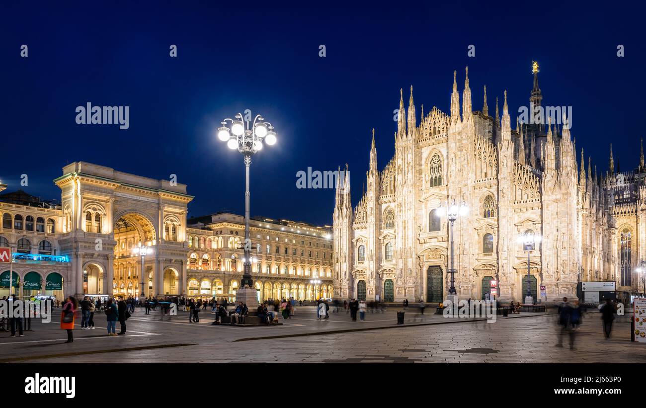 La gente disfruta de la Piazza del Duomo, dominada por la fachada de la catedral y la entrada de la galería Vittorio Emanuele II por la noche en Milán, Italia. Foto de stock