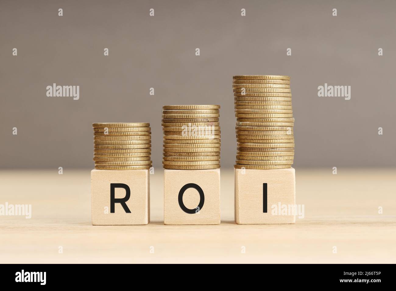 Palabra ROI en bloques de madera con monedas apiladas en pilas en aumento. Concepto de retorno de la inversión. Espacio de copia Foto de stock
