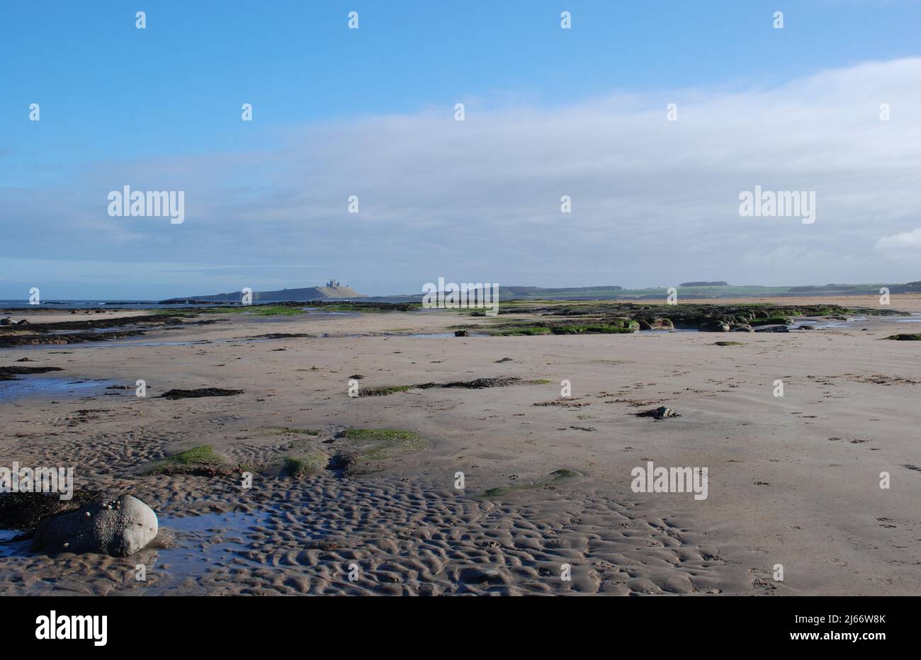 Vista del paisaje a lo largo de la playa cerca de Embleton en Northumberland con el Castillo de Dunstanburgh en la distancia lejos en su afloramiento rocoso y acantilado Foto de stock