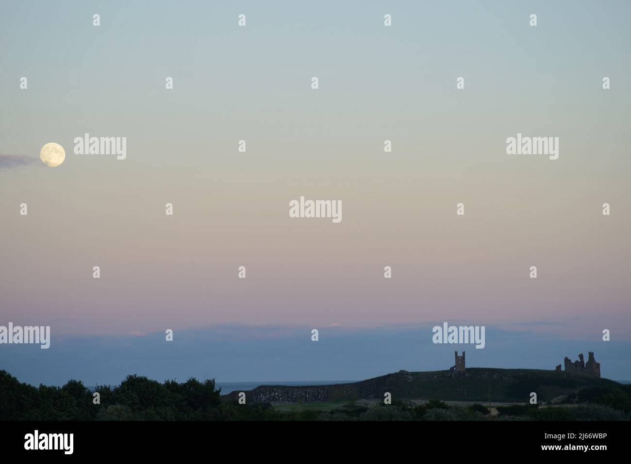 Imagen del paisaje de la luna sobre el Castillo de Dunstanburgh a primera hora de la noche a la luz del otoño Foto de stock