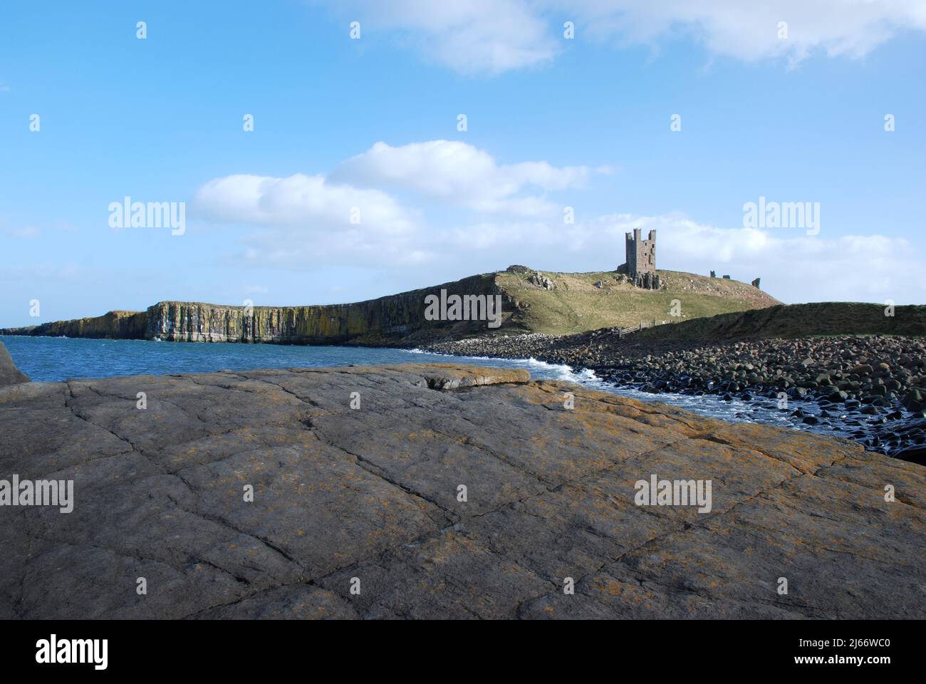 Imagen del paisaje que muestra el Castillo de Dunstanburgh en su cresta basáltica vista desde las rocas a lo largo de la costa Foto de stock