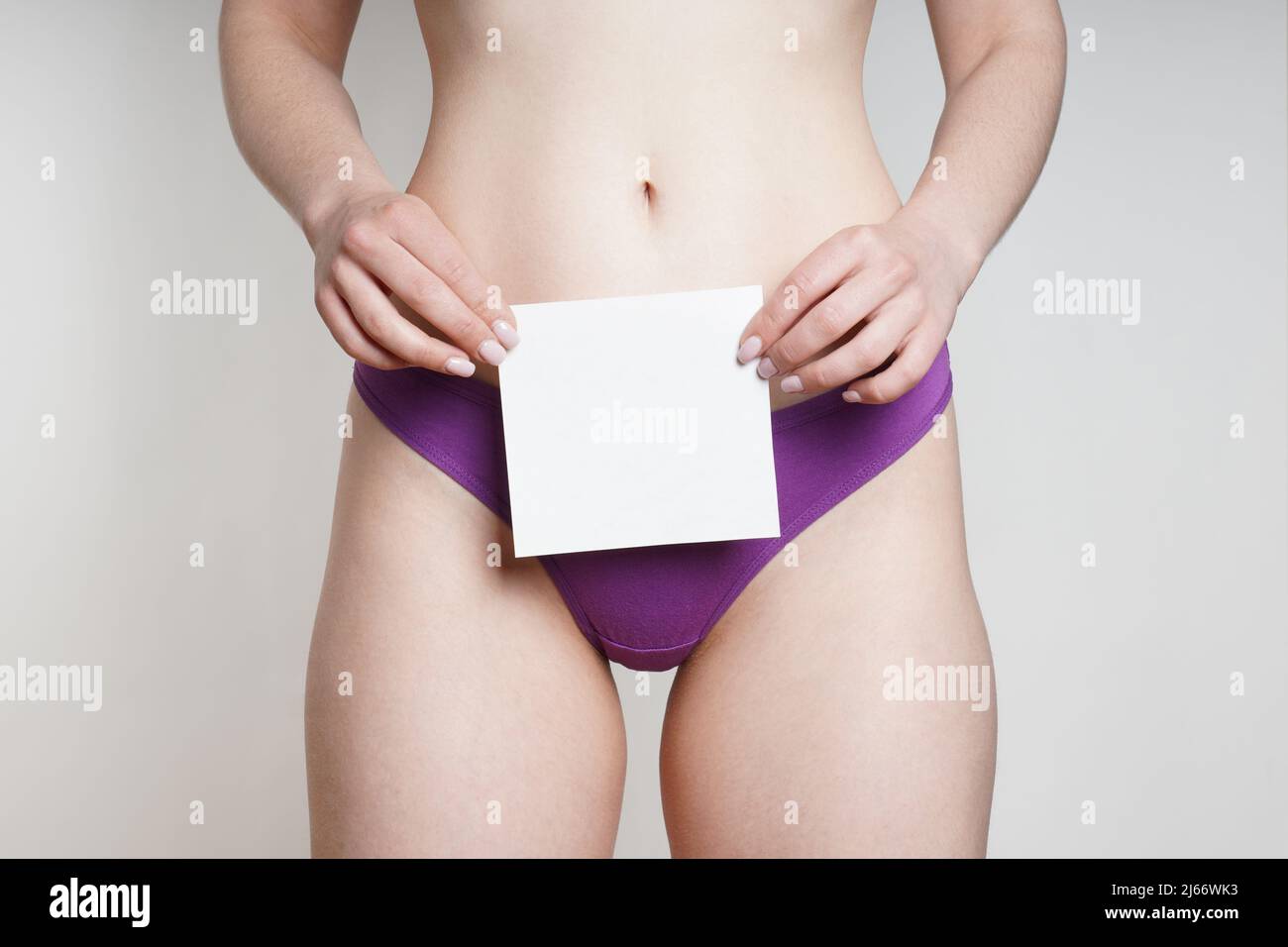 mujer en bragas sosteniendo un pedazo de papel en blanco con espacio de copia sobre el área genital Foto de stock