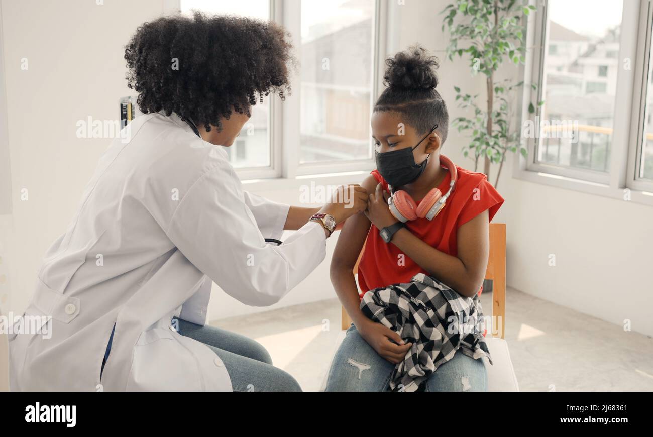 El médico afroamericano está aplicando yeso al hombro de un niño después de ser vacunado. Apertura de mangas para vacunar contra la gripe o la epidemia en HEAL Foto de stock