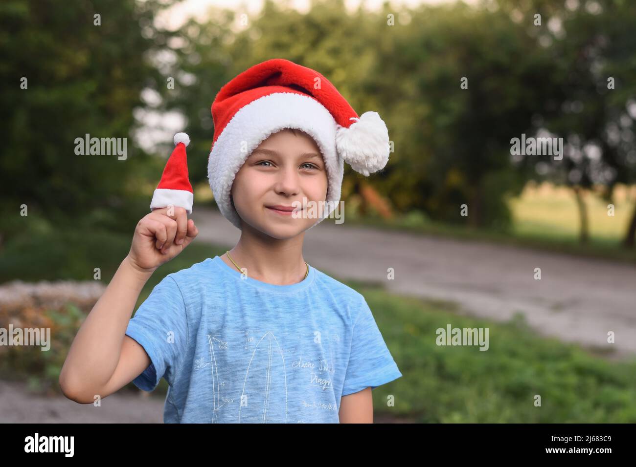 Divertido chico sonriente en el sombrero de Santa. En el verano en la calle. Sobre el fondo del follaje verde. Foto de stock