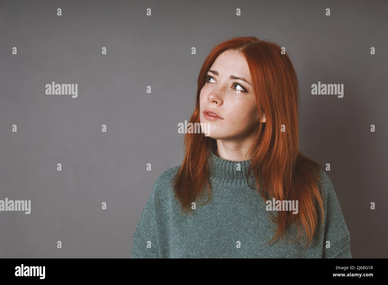 una mujer pensativa en el suéter de cuello de cisne está mirando para arriba pensando o planeando Foto de stock