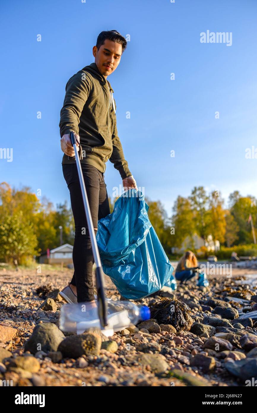 Voluntario recogiendo basura con un gancho en la playa Foto de stock