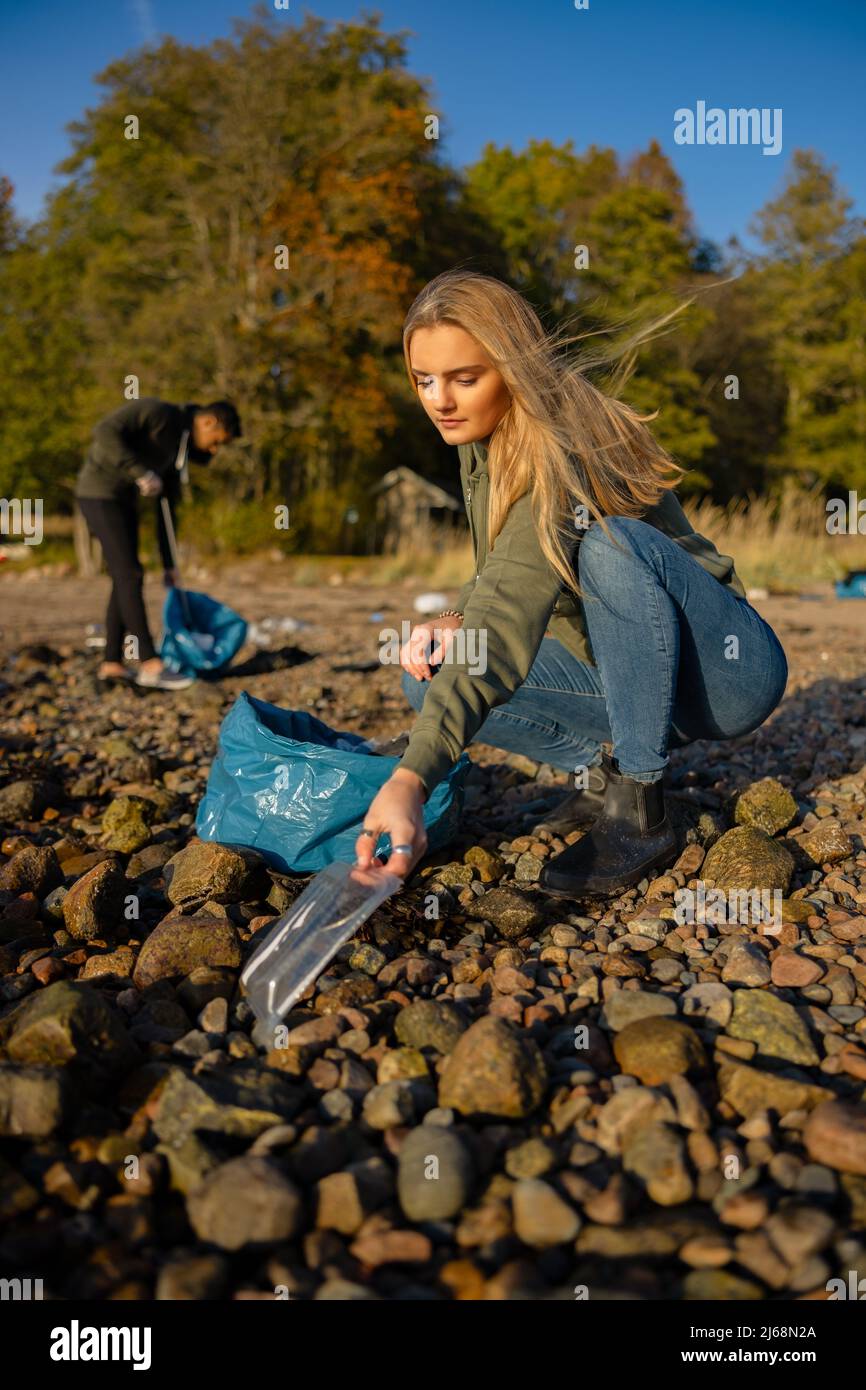 Una joven seria en el equipo de conservación del medio ambiente recogiendo plástico en la playa Foto de stock