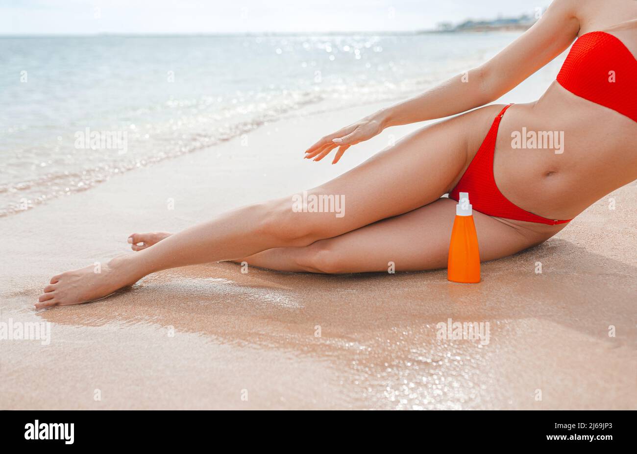Niña usando protector solar y tumbada en la playa junto al océano o al mar Mujer aplicando crema solar sobre el cuerpo bronceado para proteger su piel. Hembra de retención de sol lote Foto de stock
