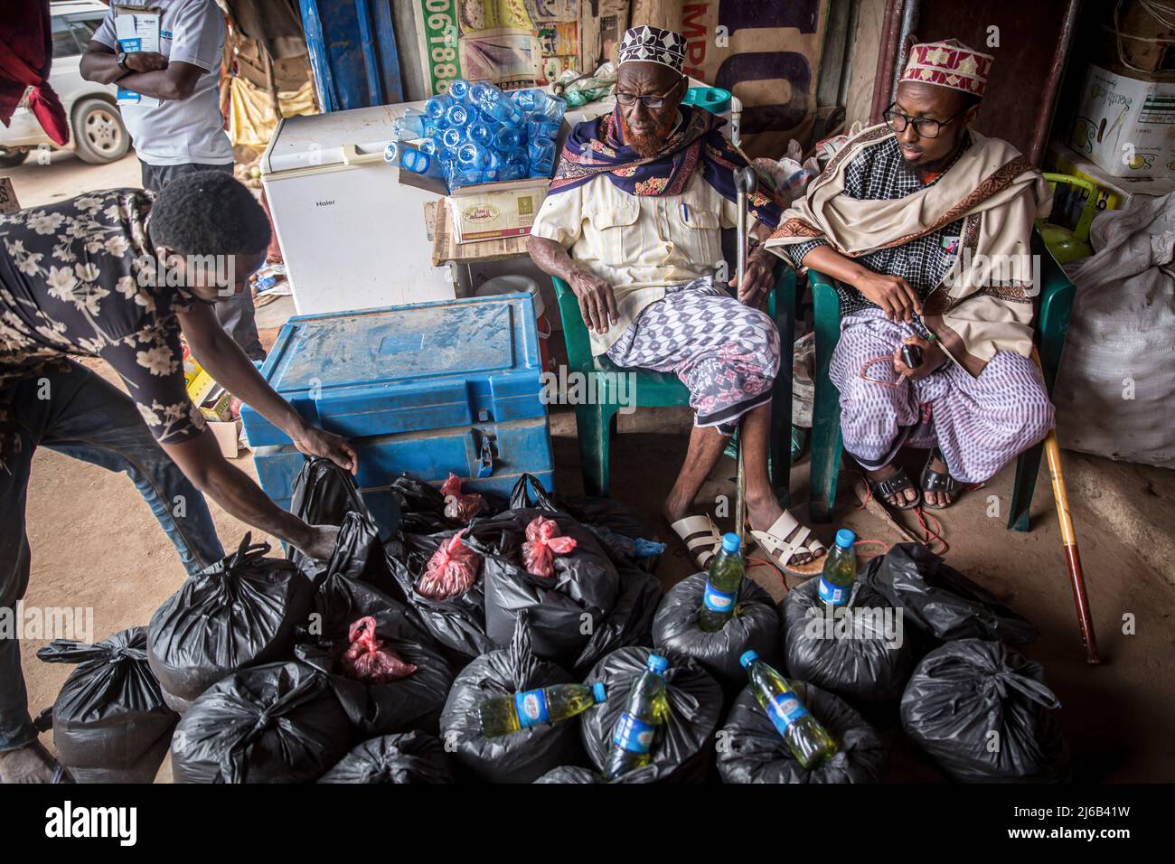 Los hombres somalíes reúnen paquetes de arroz, aceite de cocina y otros artículos esenciales para las familias necesitadas en el exterior de una tienda en Dollow, Jubaland, en el suroeste de Somalia. Foto de stock