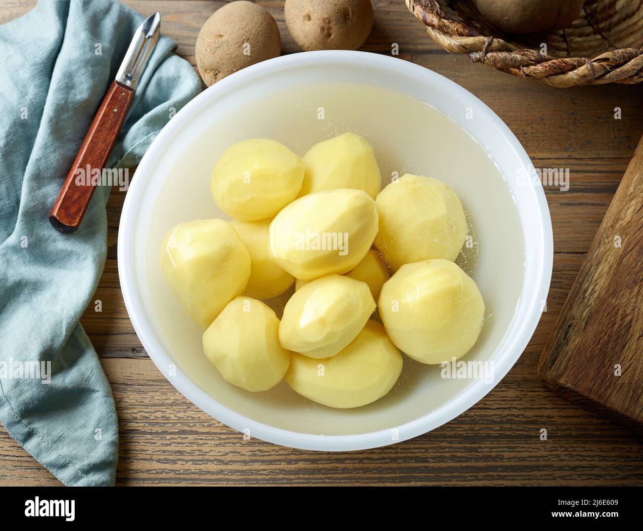 patatas frescas peladas crudas en un tazón de agua fría en una mesa de cocina de madera, vista superior Foto de stock