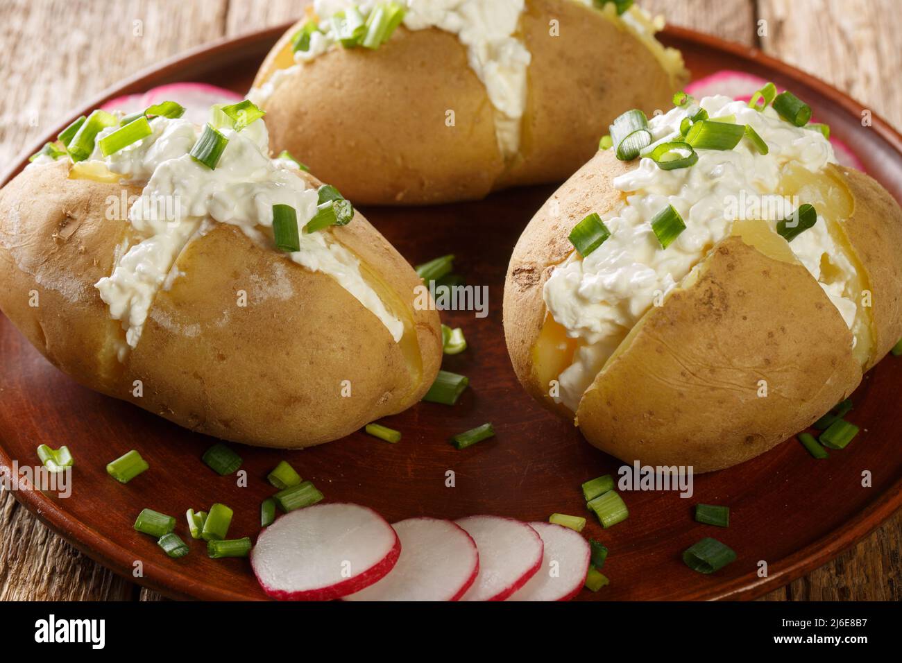 Patatas a la chaqueta hervidas rellenas de queso cottage, crema agria y  cebollas verdes en primer plano en un plato sobre una mesa de madera.  Horizontal Fotografía de stock - Alamy