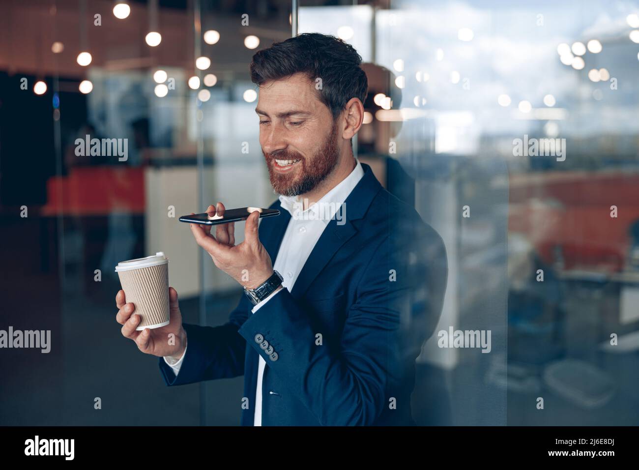 Un hombre de negocios guapo está utilizando un smartphone para grabar un mensaje de voz al socio comercial Foto de stock