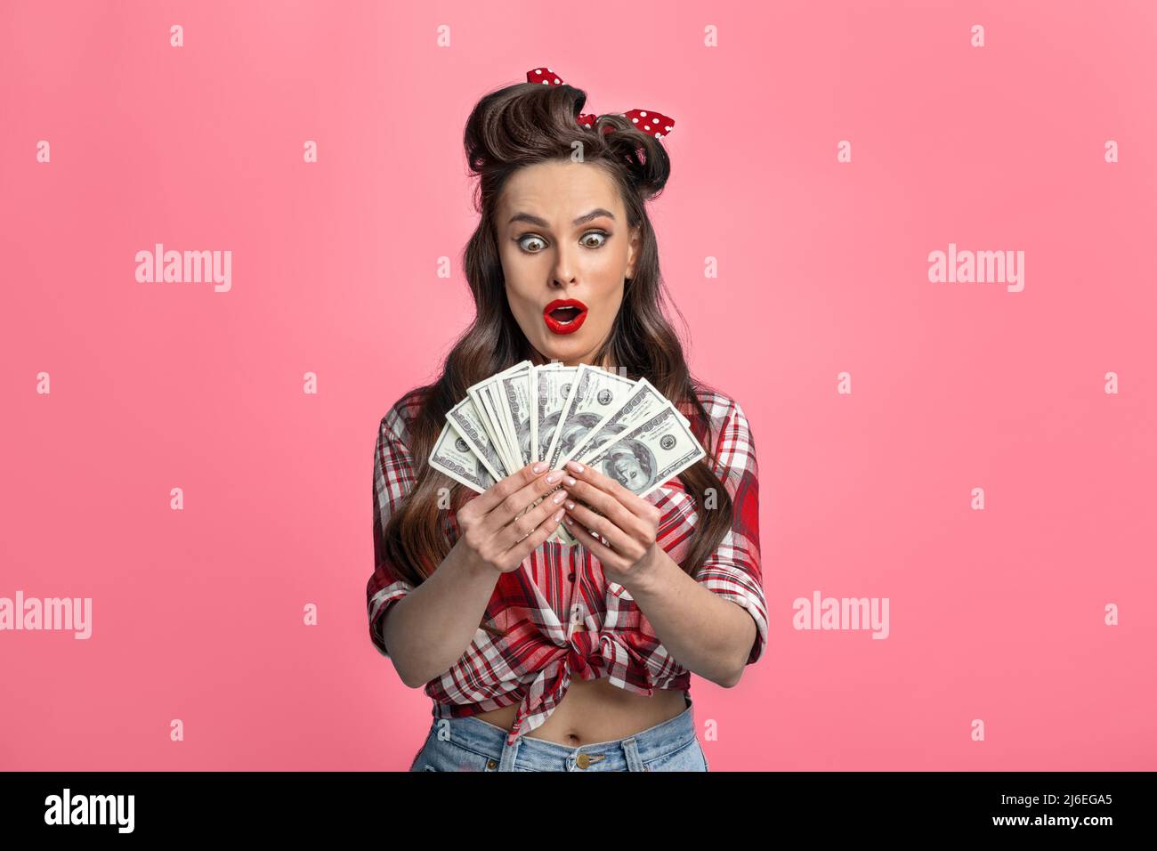 Emocionado millennial pinup dama en estilo retro de uso que sostiene a fan del dinero, ganar en línea apuesta de casino o lotería Foto de stock