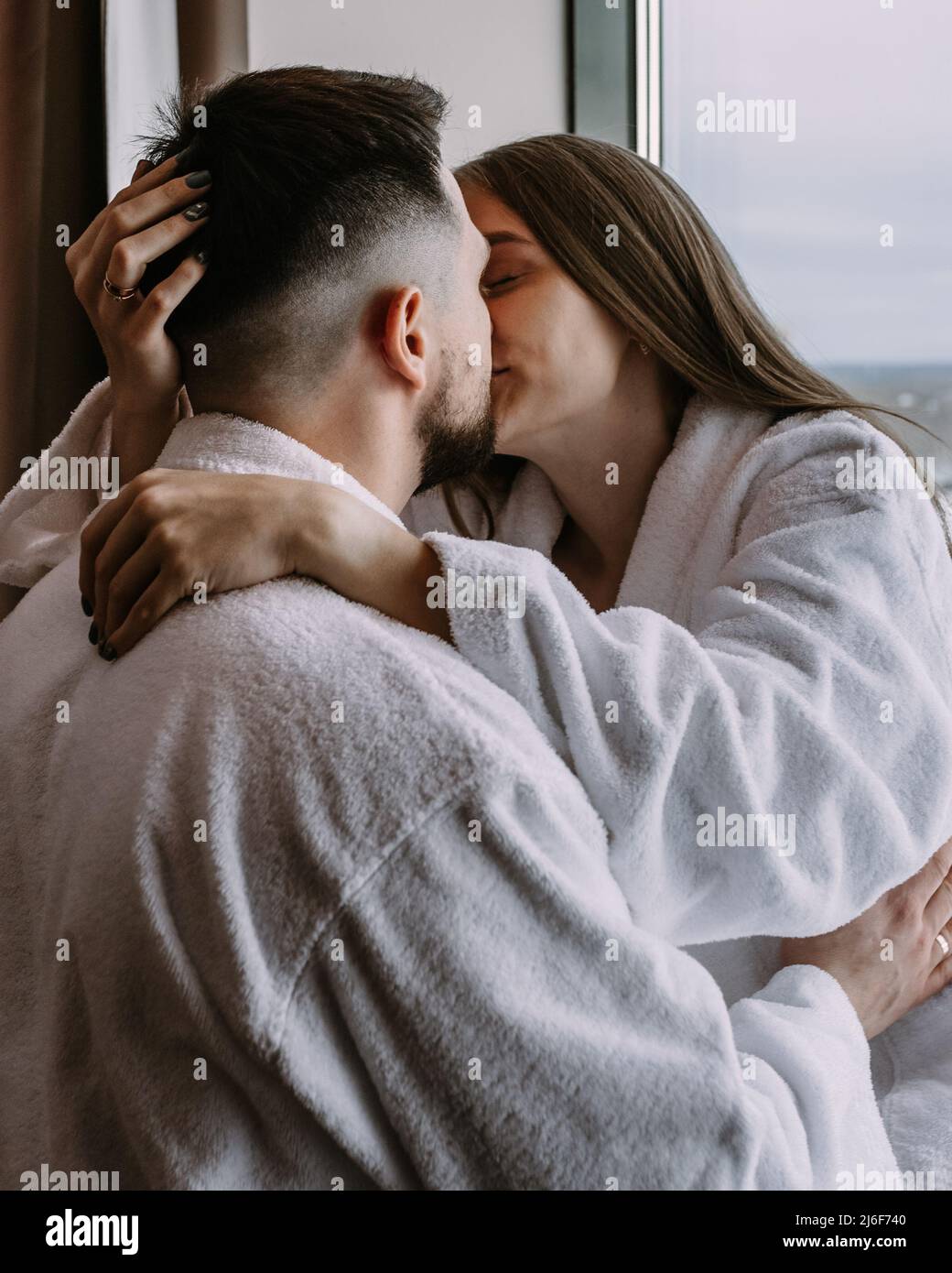 Feliz pareja hermosa en el hotel en la ventana besarse y abrazarse unos a otros Foto de stock