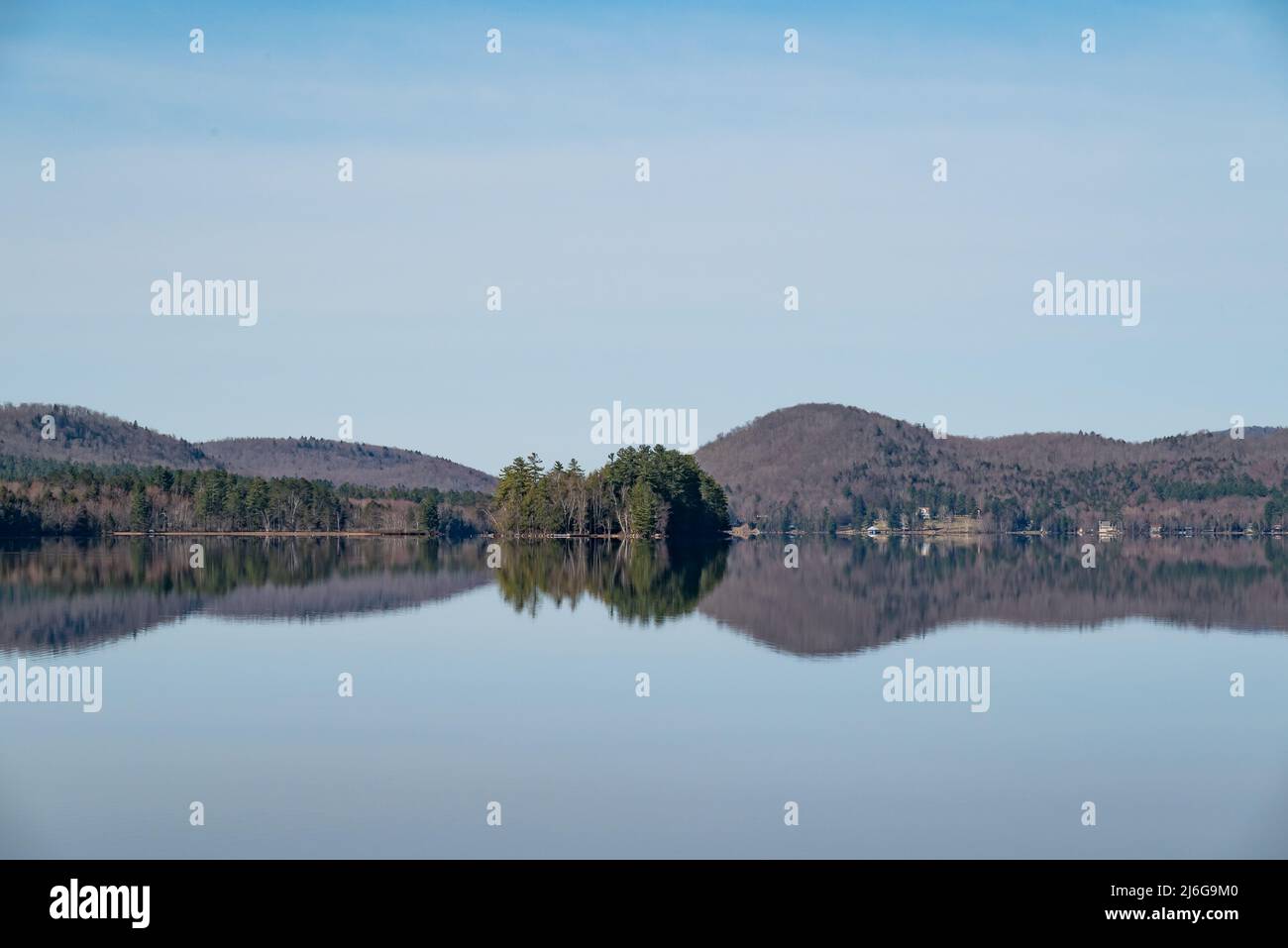 Una vista del Lago Pleasant en las Montañas Adirondack en un día claro y tranquilo con la isla Tapawingo y la distante costa reflejada en el agua Foto de stock