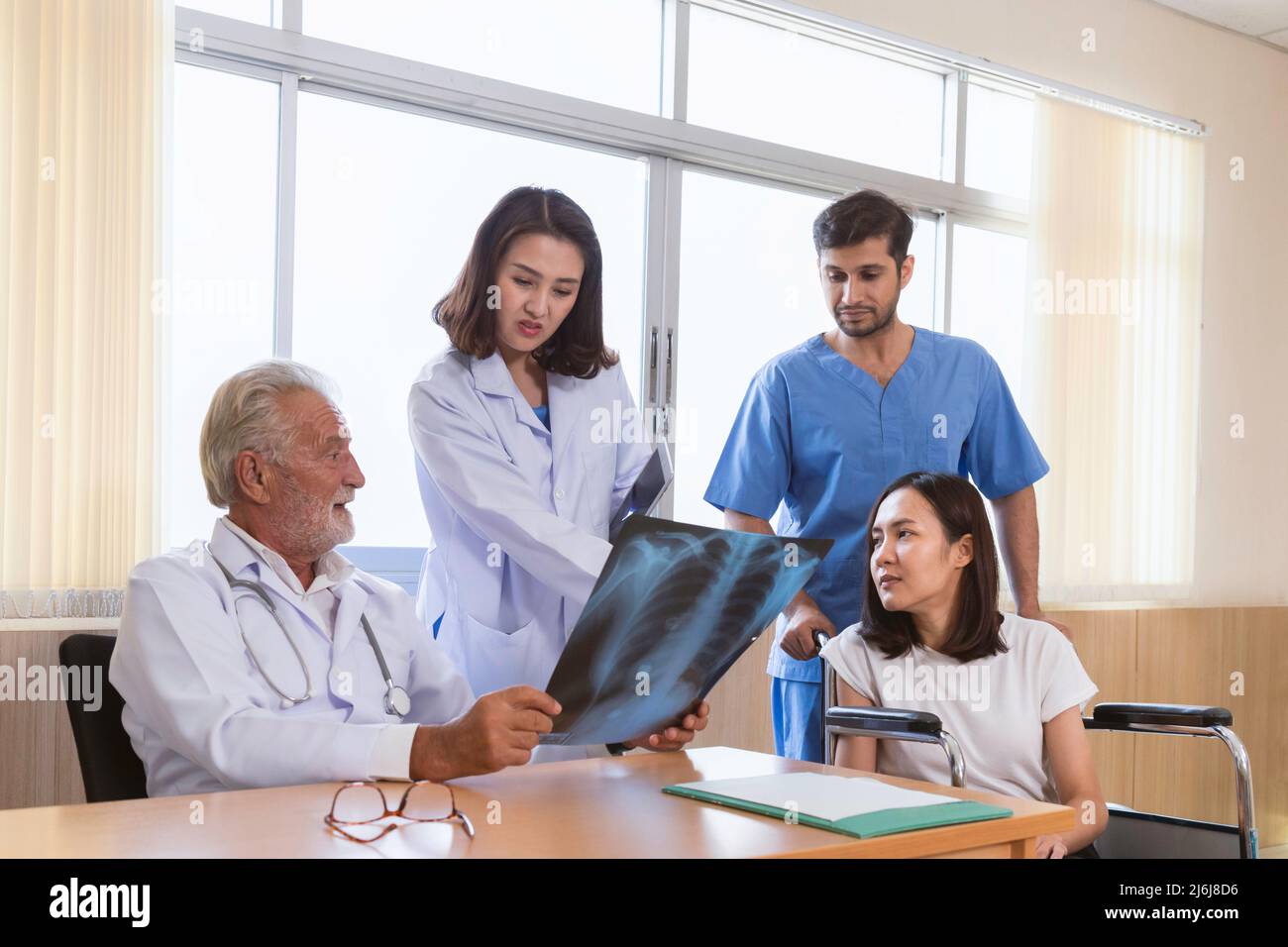 médicos cirujanos senior que muestran una película de rayos x para pacientes femeninos para hablar y consultar con una joven doctora y equipo antes de la cirugía en el hos Foto de stock